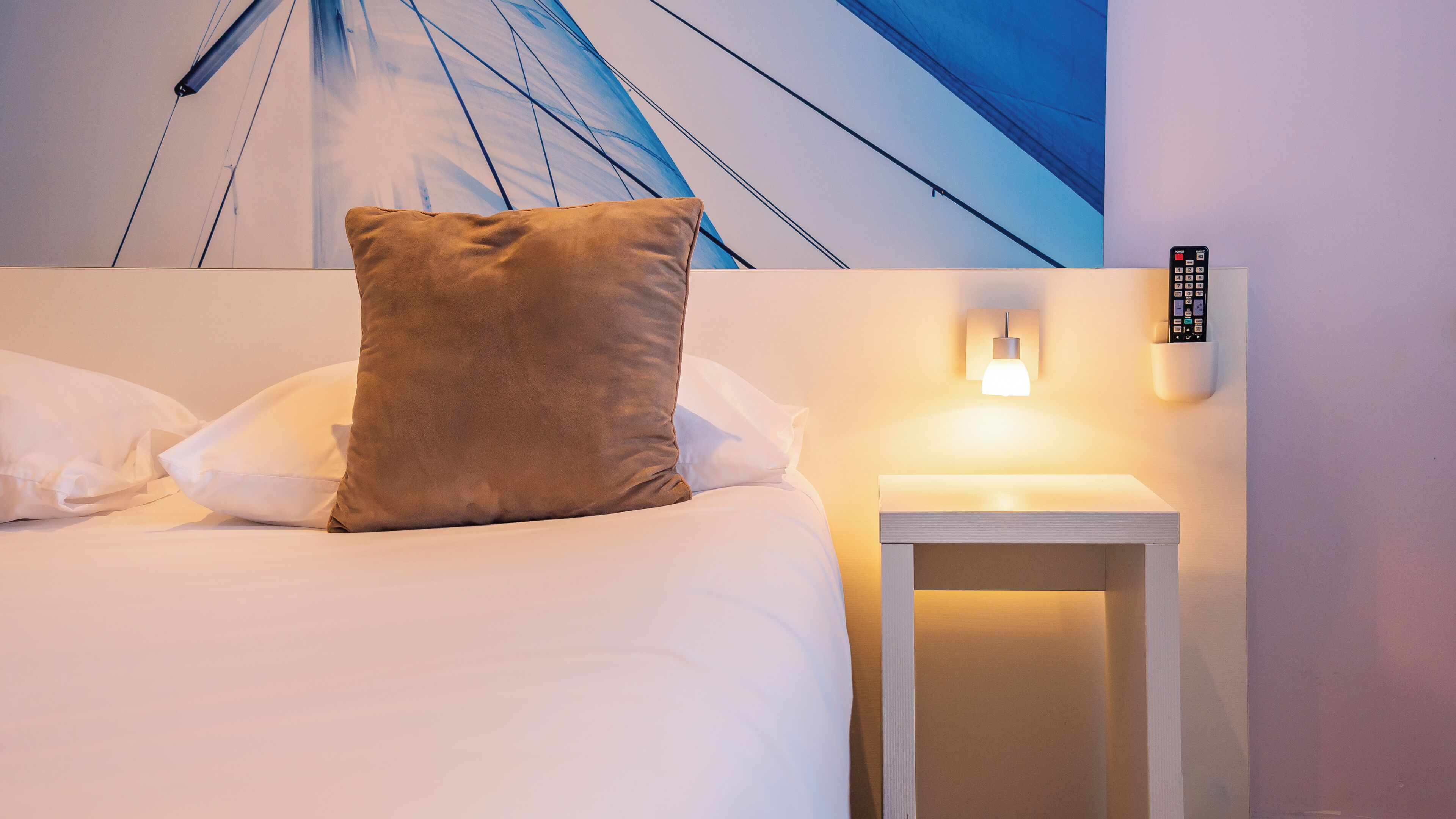 Una habitación de hotel con una cama, una mesita de noche con lámpara y un control remoto fijado a la pared.
