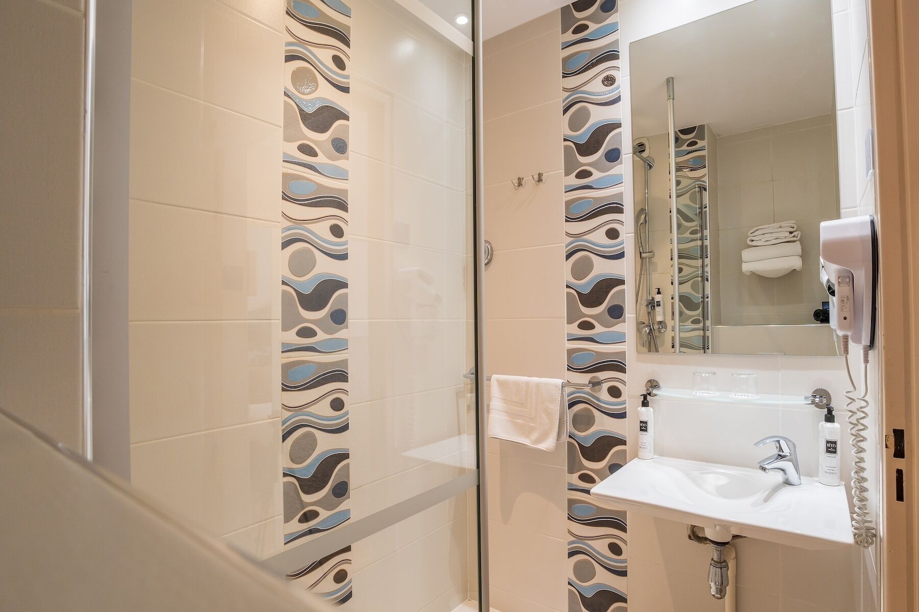 A bathroom with a glass shower enclosure, a white sink with a mirror above it, and a towel rack with a folded towel.