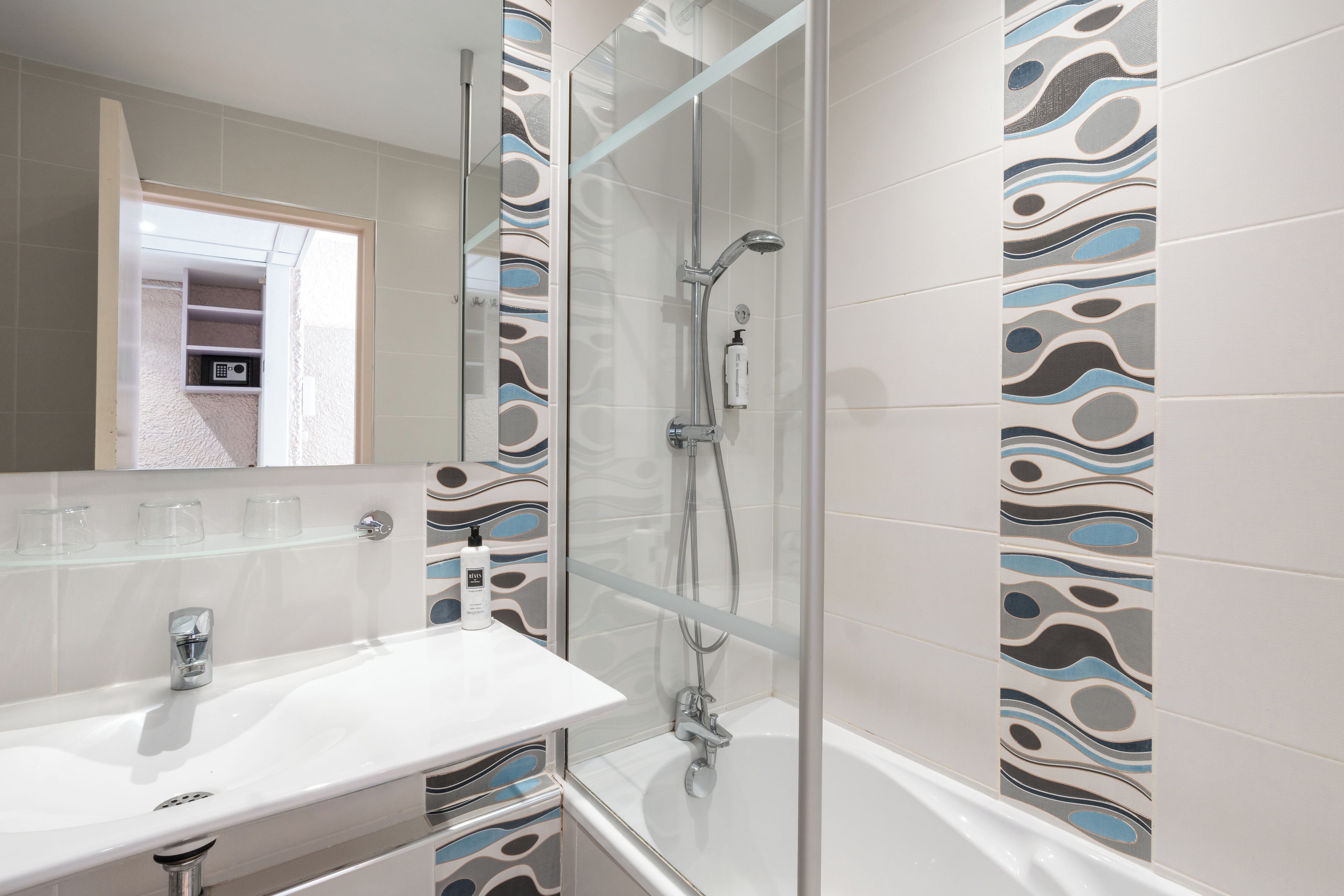 A modern bathroom with a glass shower enclosure, a white sink, and patterned tiles.