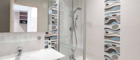 A modern bathroom with a glass shower enclosure, a white sink, and patterned tiles.