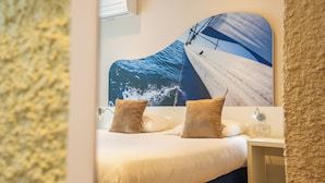 A hotel room with a large ocean-themed mural on the wall, a bed with white bedding and two pillows, a small bedside table with a lamp, and a wall-mounted air conditioning unit. - Hôtel Europe (La Grande-Motte)