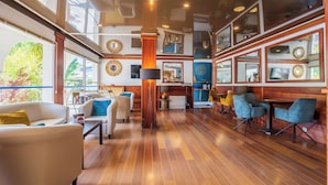 A spacious, well-lit interior with wooden flooring, comfortable seating, and large windows offering views of greenery. - Hôtel Europe (La Grande-Motte)