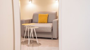 Un sillón moderno con un cojín amarillo, una mesita redonda y un suelo de tonos claros.