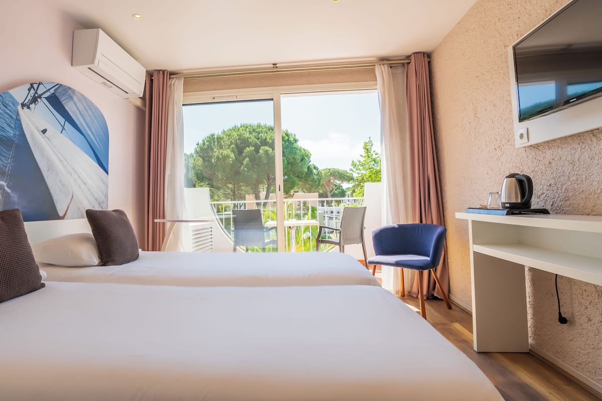A hotel room with a large bed, a desk with a kettle, a TV, and a view of the outdoors.