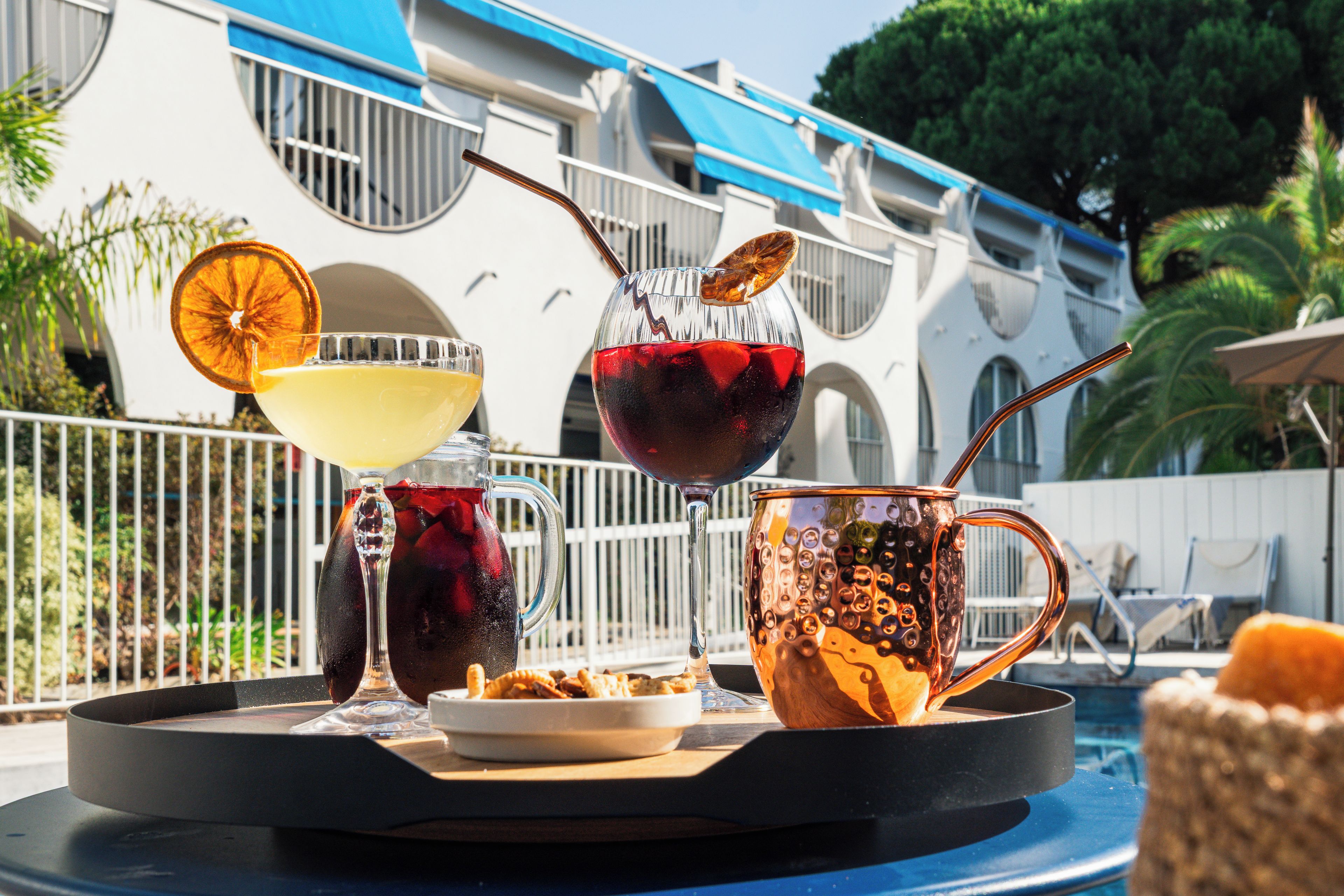 Una bandeja con bebidas y aperitivos sobre una mesa junto a la piscina.