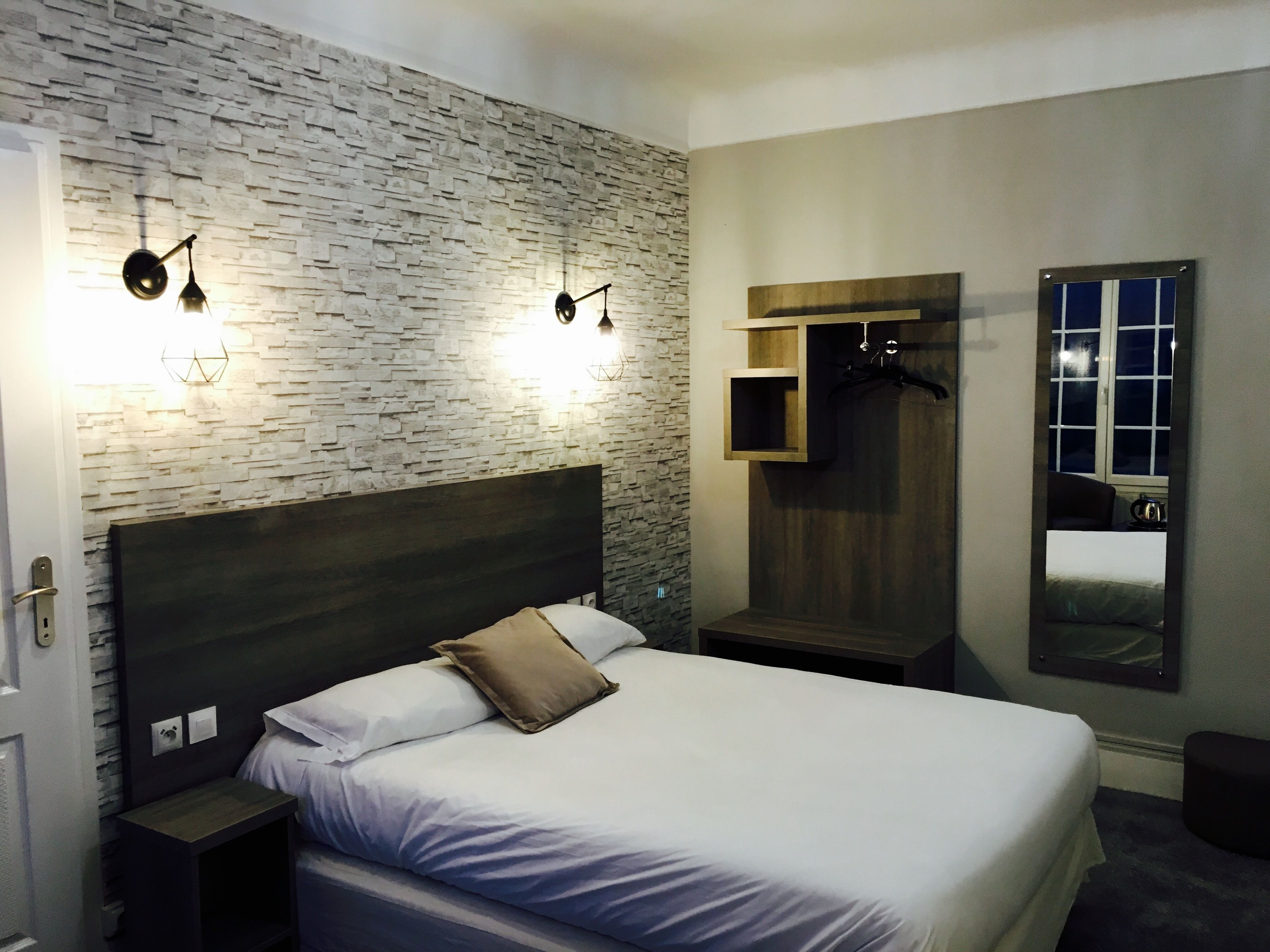 A modern bedroom with a stone-textured wall, a large bed with white bedding, a wooden headboard, and built-in lighting fixtures.