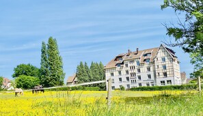 A large building with multiple windows and a sloped roof, surrounded by a field of yellow flowers. - Sure Hotel by Best Western Port Jérome - Le Havre (Port-Jérôme-sur-Seine)