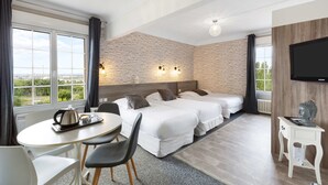 Habitación de hotel con dos camas, una mesa de comedor, televisor y vistas al exterior.