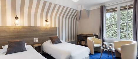 Habitación de hotel con dos camas, un escritorio, una silla, una mesita con hervidor y un amplio ventanal con cortinas.