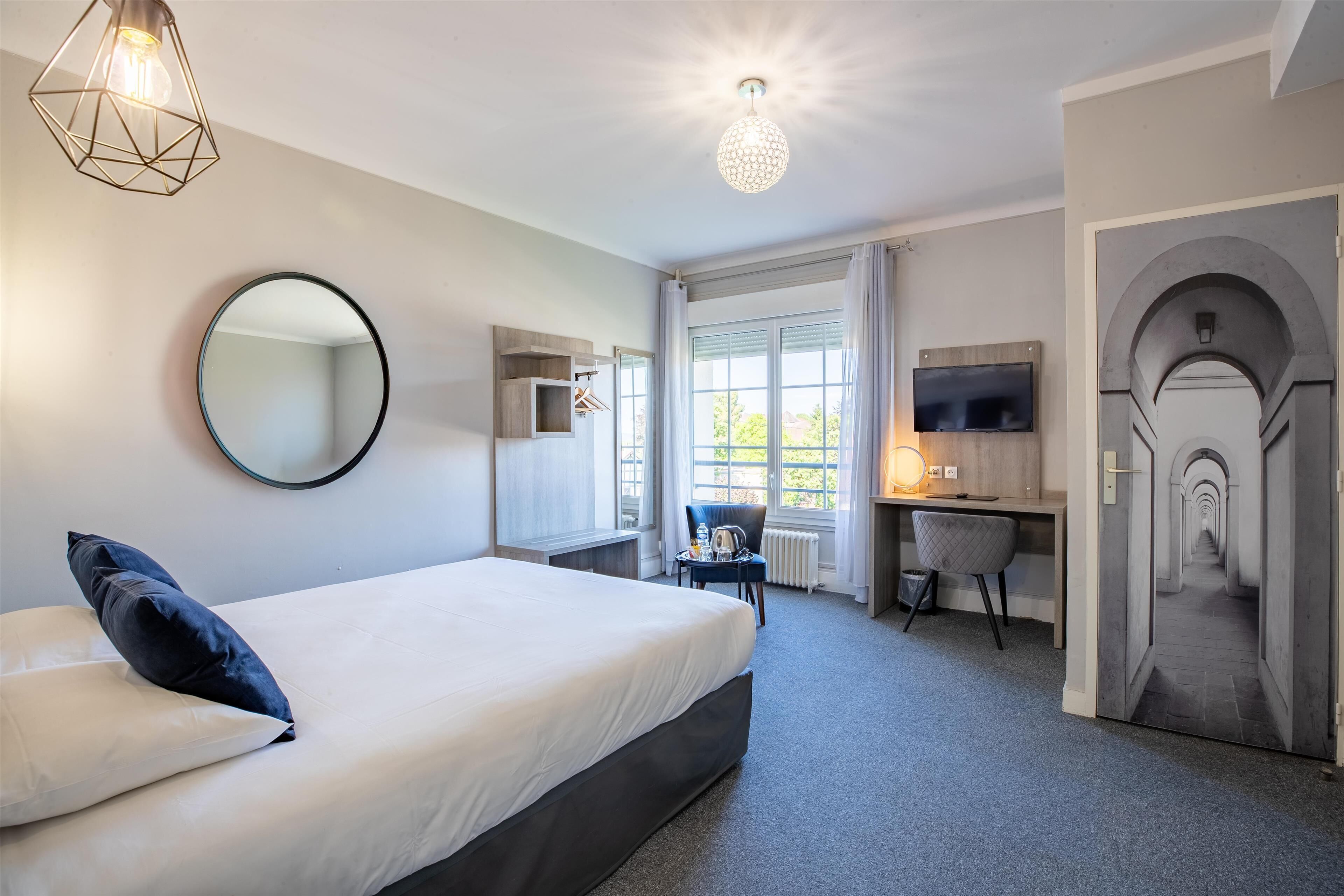 Une chambre d’hôtel moderne équipée d’un grand lit, d’un bureau, d’une chaise, d’une télévision et d’un miroir.