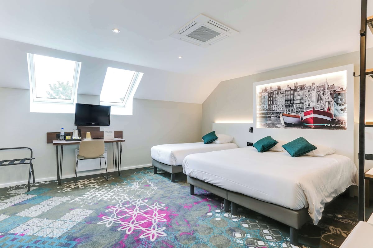 Une chambre d’hôtel avec deux lits, un bureau avec une chaise, une télévision et une grande fenêtre.
