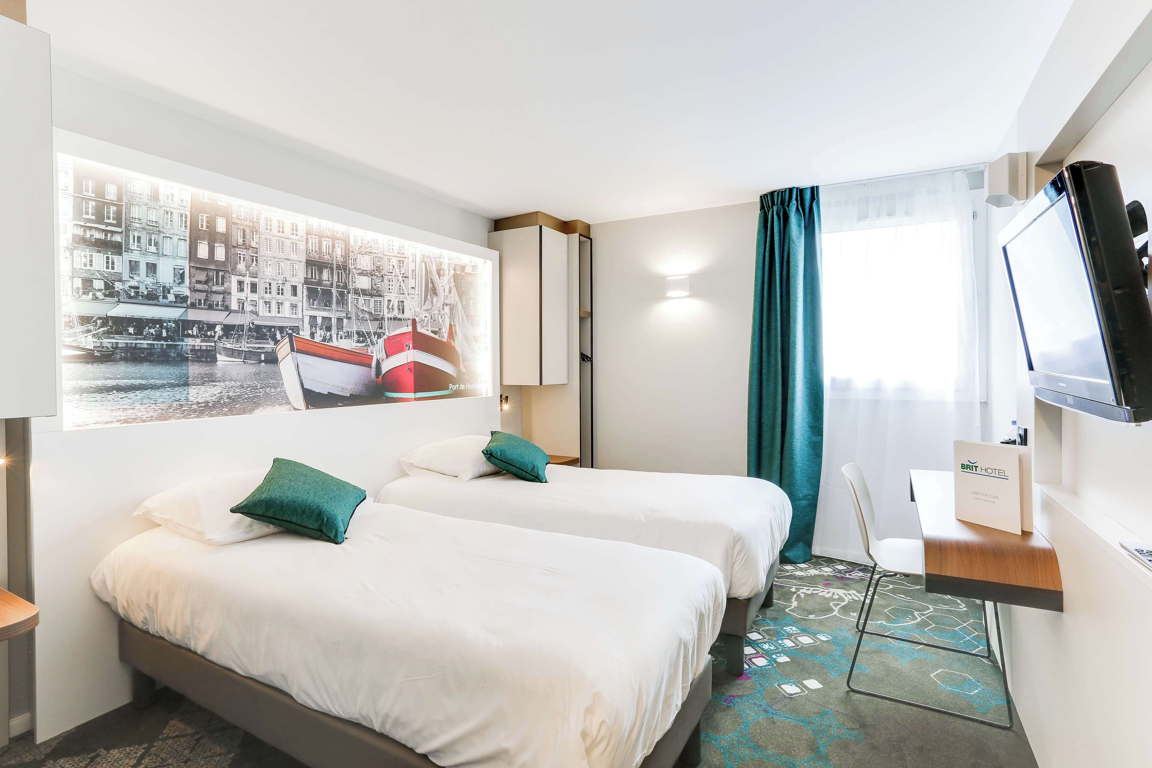 Ein Hotelzimmer mit zwei Betten, einem Fernseher, einem Schreibtisch und einem Stadtbild.