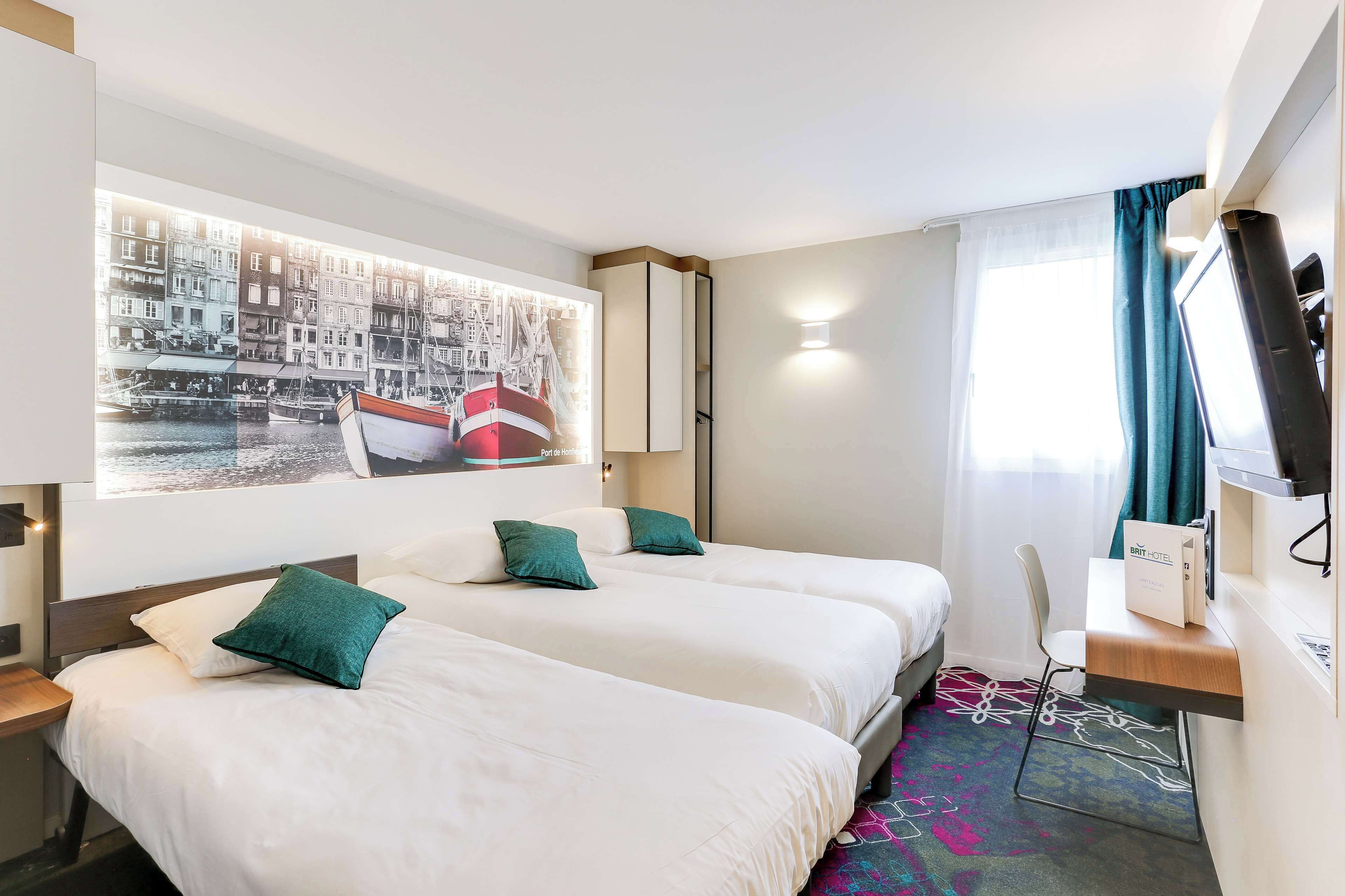 A hotel room with two beds, a desk, a TV, and a large window with curtains.