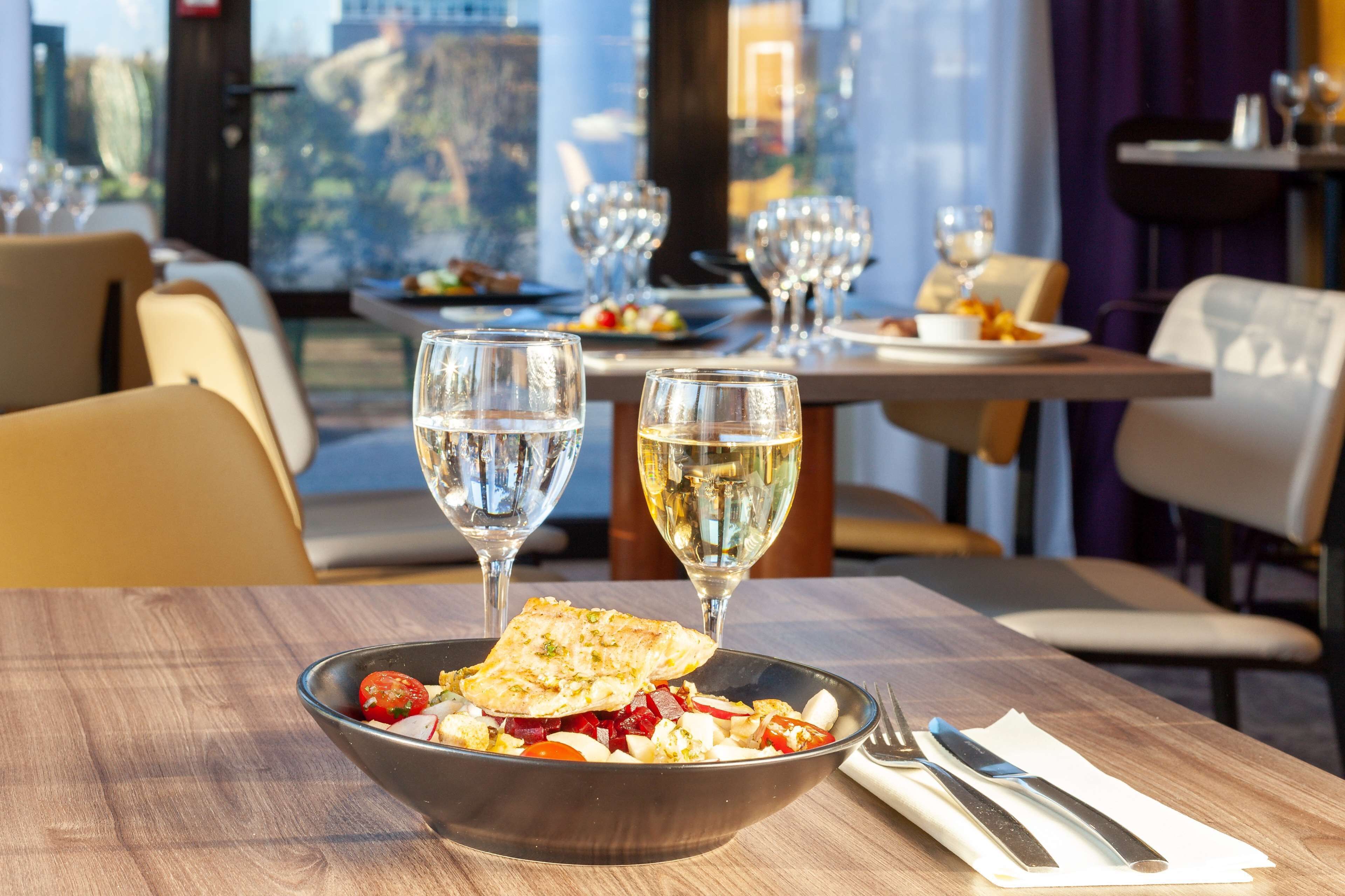 A dining table with a bowl of food, two wine glasses, and a set of cutlery.