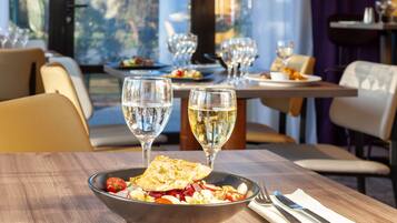 A dining table with a bowl of food, two wine glasses, and a set of cutlery.