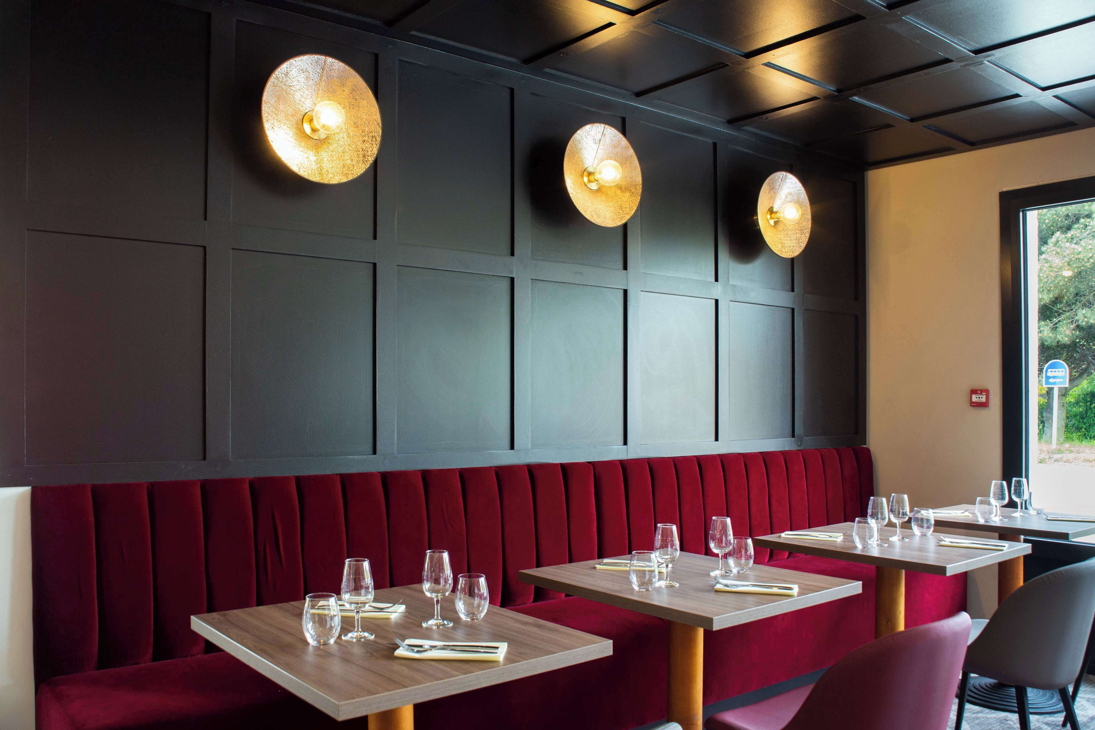 Interior de restaurante com cabines estofadas em vermelho, mesas de madeira e iluminação pendente.