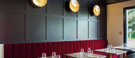 Interior de restaurante con asientos tapizados en rojo, mesas de madera e iluminación colgante.