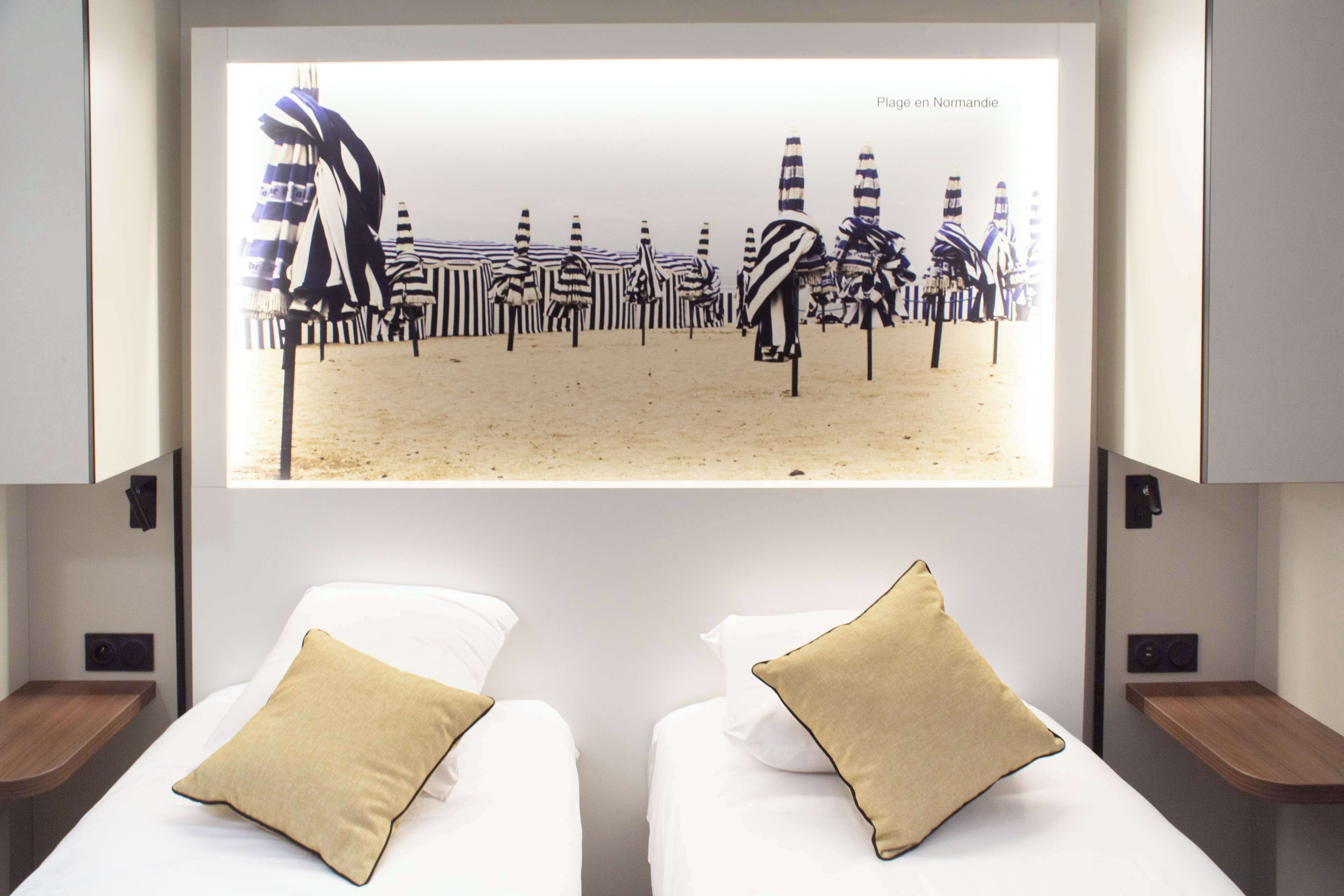 A hotel room with two beds, each with a beige pillow, and a large screen displaying striped beach umbrellas.
