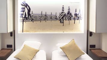 A hotel room with two beds, each with a beige pillow, and a large screen displaying striped beach umbrellas.