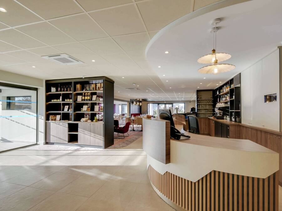 Un moderno vestíbulo de hotel con un mostrador de recepción, zona de estar y estanterías con diversos artículos.