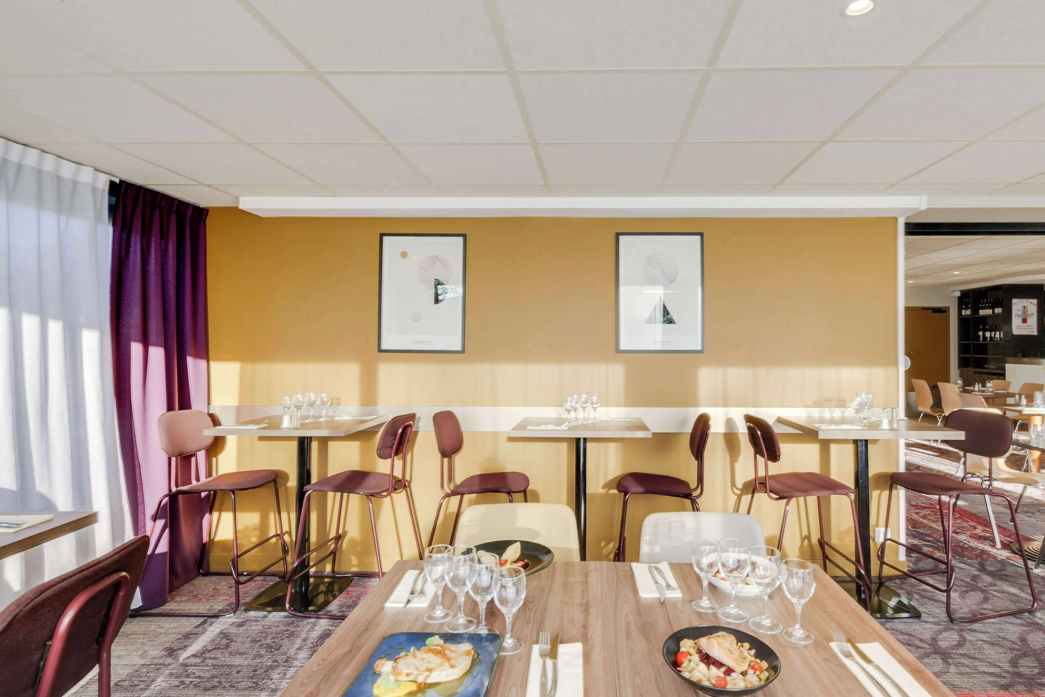 A dining area with tables and chairs, framed artwork on the walls, and a patterned carpet.