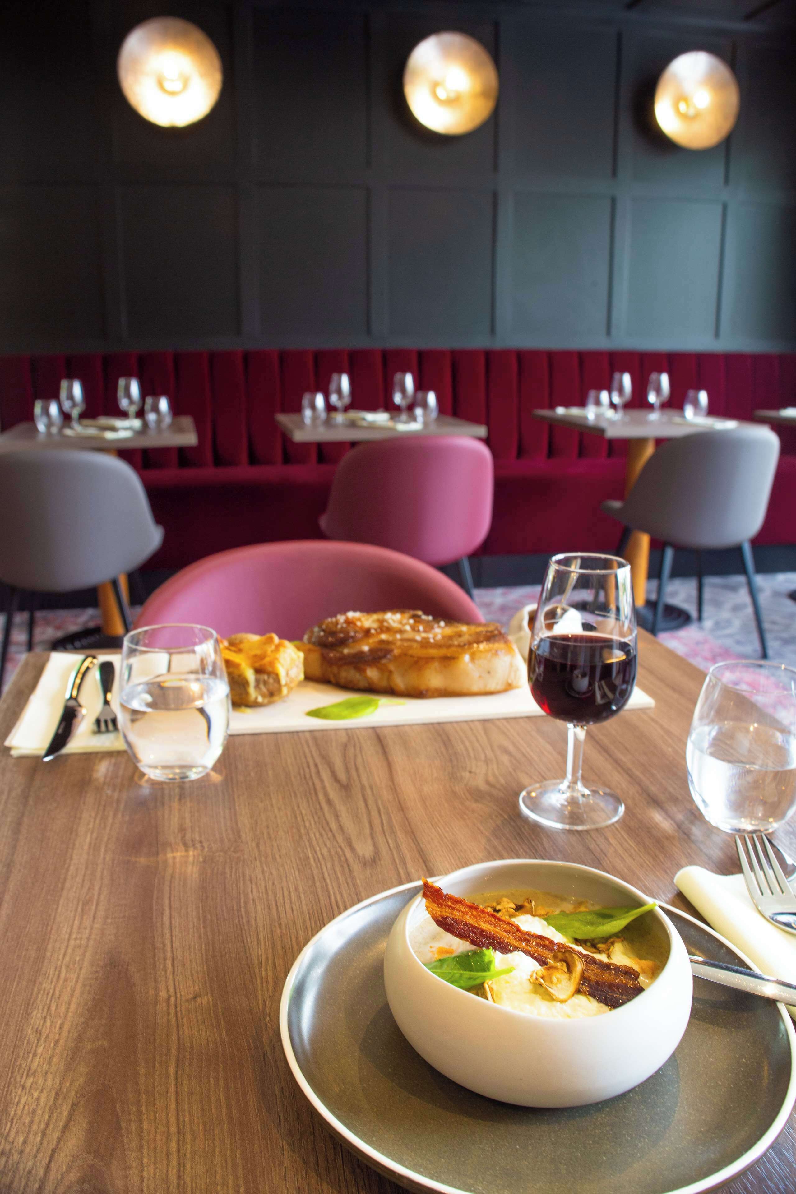 Una mesa de comedor con un plato de comida, una copa de vino tinto y un bol de sopa.