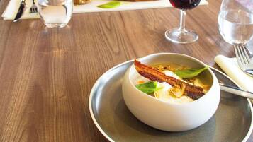 Una mesa de comedor con un plato de comida, una copa de vino tinto y un bol de sopa.