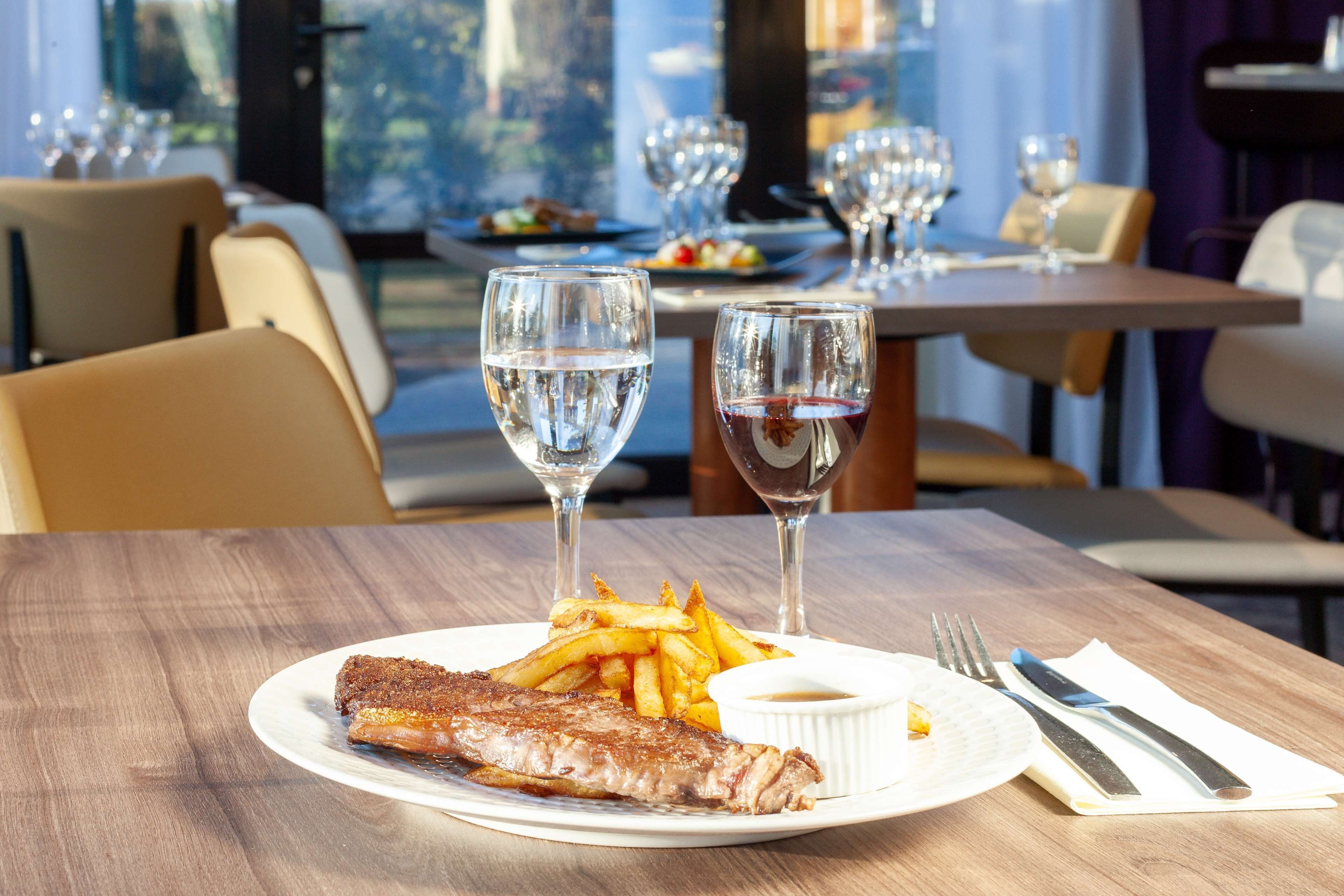 Ett matbord med en tallrik med biff och pommes frites, två glas vatten och en liten skål med sås.