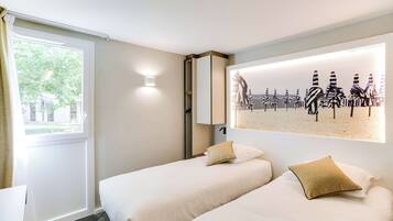 Une chambre d’hôtel avec deux lits, une grande fenêtre et une œuvre d’art accrochée au mur représentant des parasols à rayures.