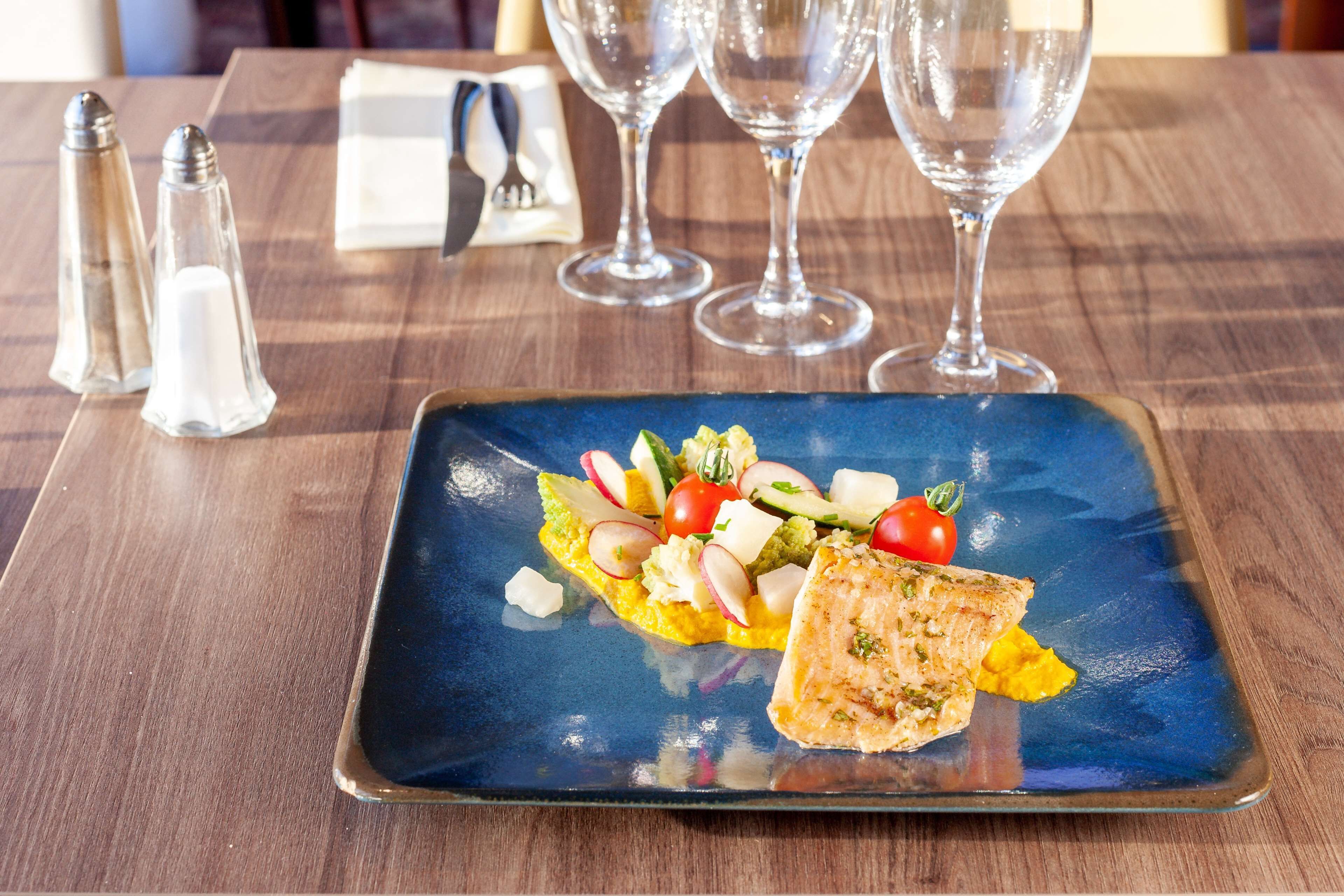 A square plate with a salad and a piece of grilled fish on a blue ceramic plate.