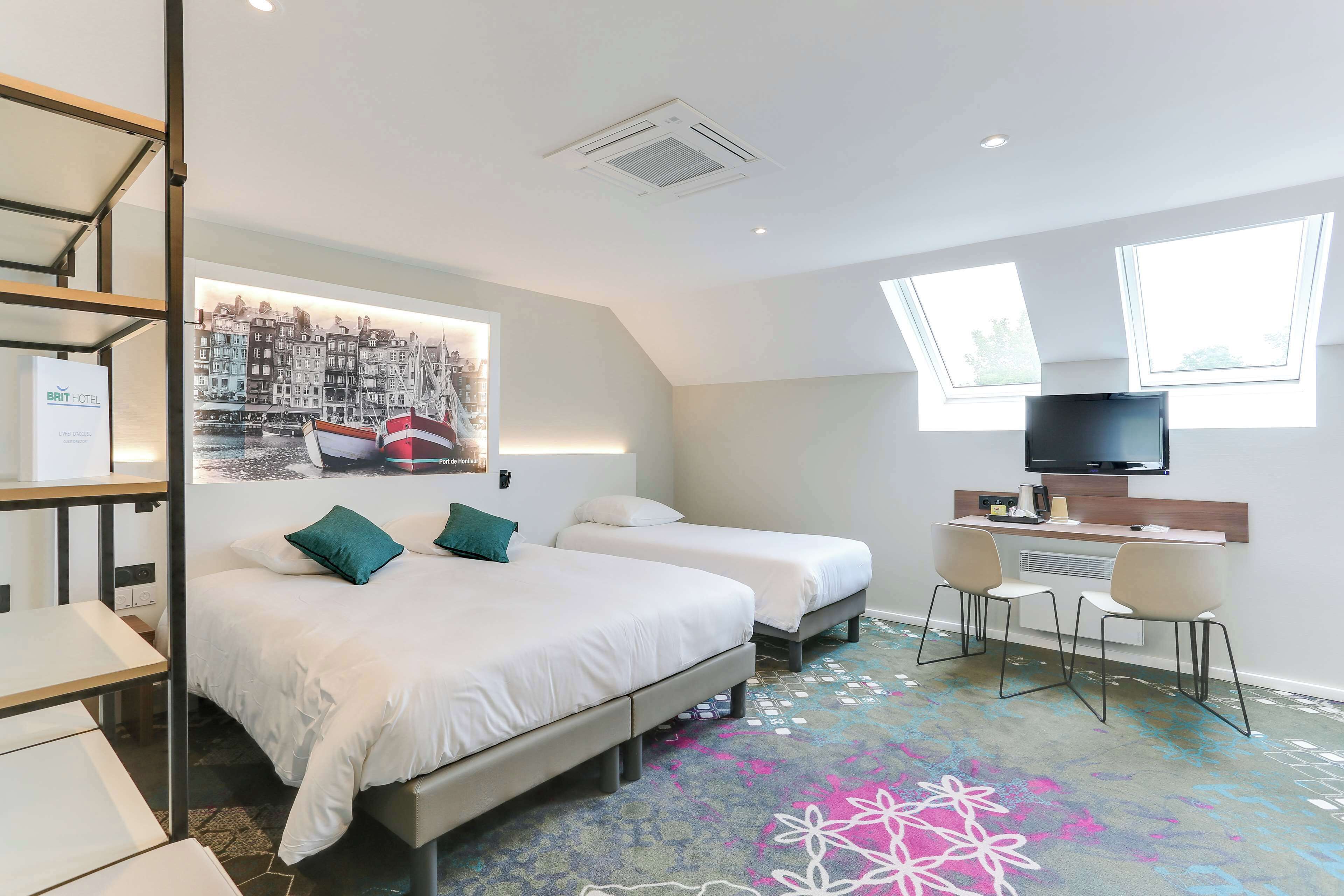 A hotel room with two beds, a desk, a television, and a large window.