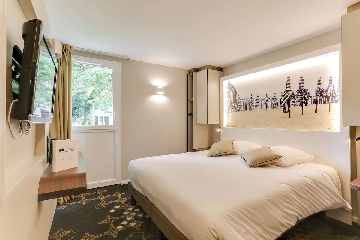 Une chambre d’hôtel équipée d’un lit, d’une télévision, d’une fenêtre avec des rideaux, d’une œuvre d’art accrochée au mur et d’une pancarte indiquant le type de chambre.