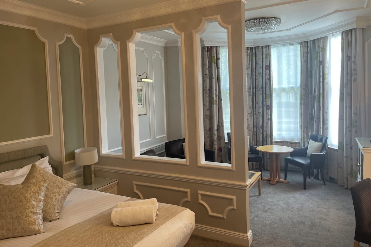 A hotel room with a large bed, a sitting area with a table and chairs, and a view of the outdoors through curtains.