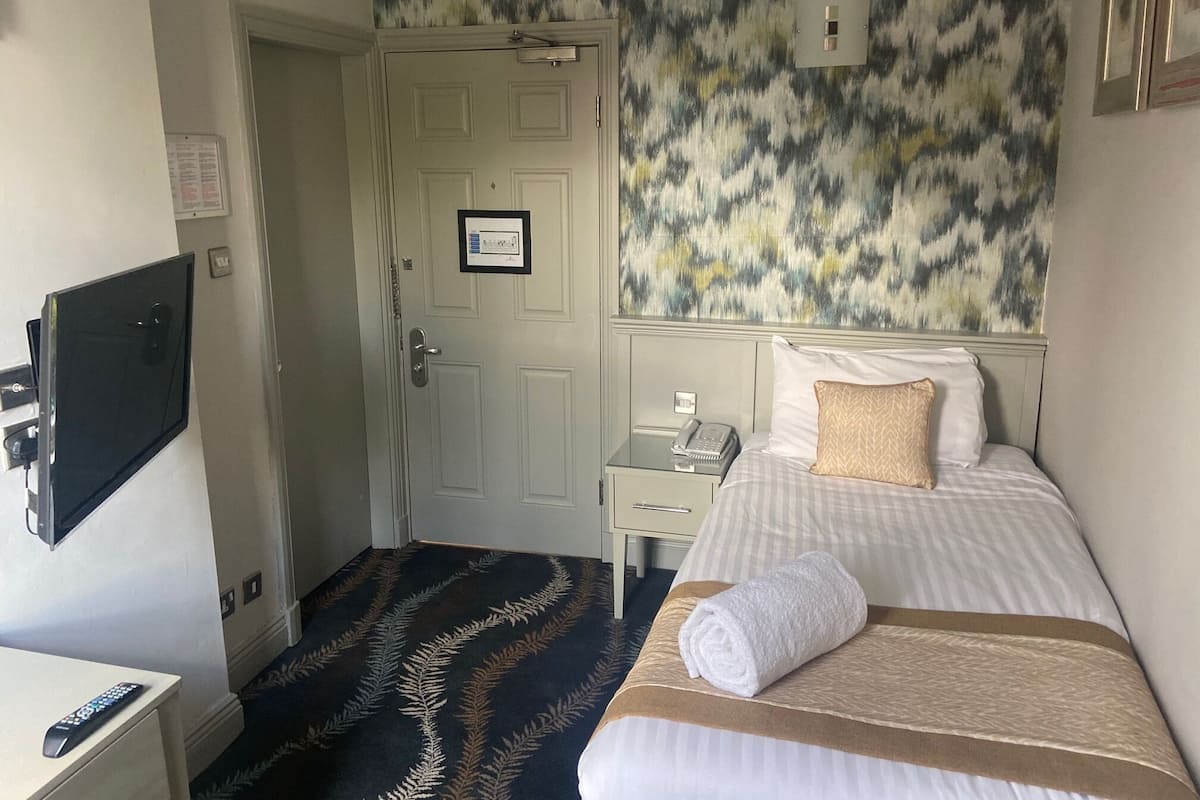 A hotel room with a bed, a bedside table with a phone, a TV mounted on the wall, and a door with a framed certificate.