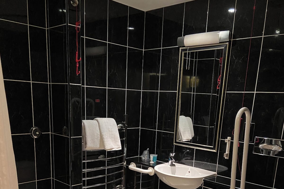 A modern bathroom with black tiles, a white sink, a mirror, a toilet, and a shower area.