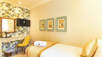 A hotel room with a bed, a desk with a mirror, a television, and three framed pictures on the wall.