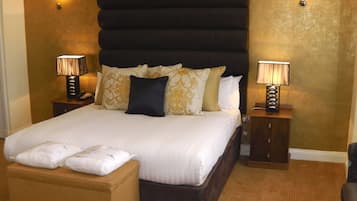 Ett hotellrum med en stor säng, två sängbord med lampor, en liten pall och en väggmonterad lampa.