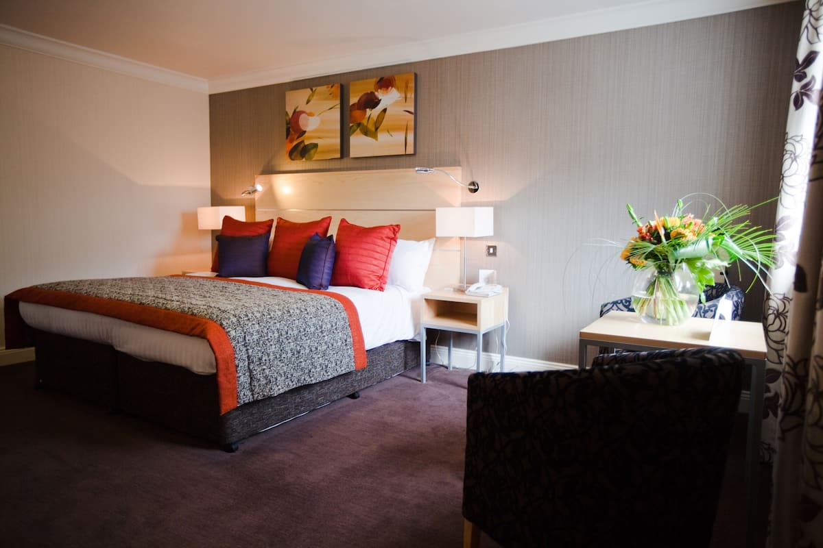 A hotel room with a bed, bedside tables, a chair, and a vase with flowers.