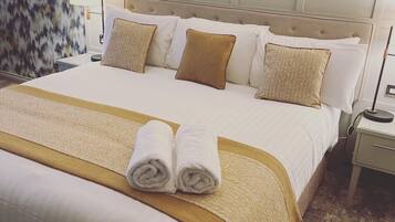 Una cama bien hecha con una colcha beige y blanca, dos toallas enrolladas y un cabecero con diseño de panel.