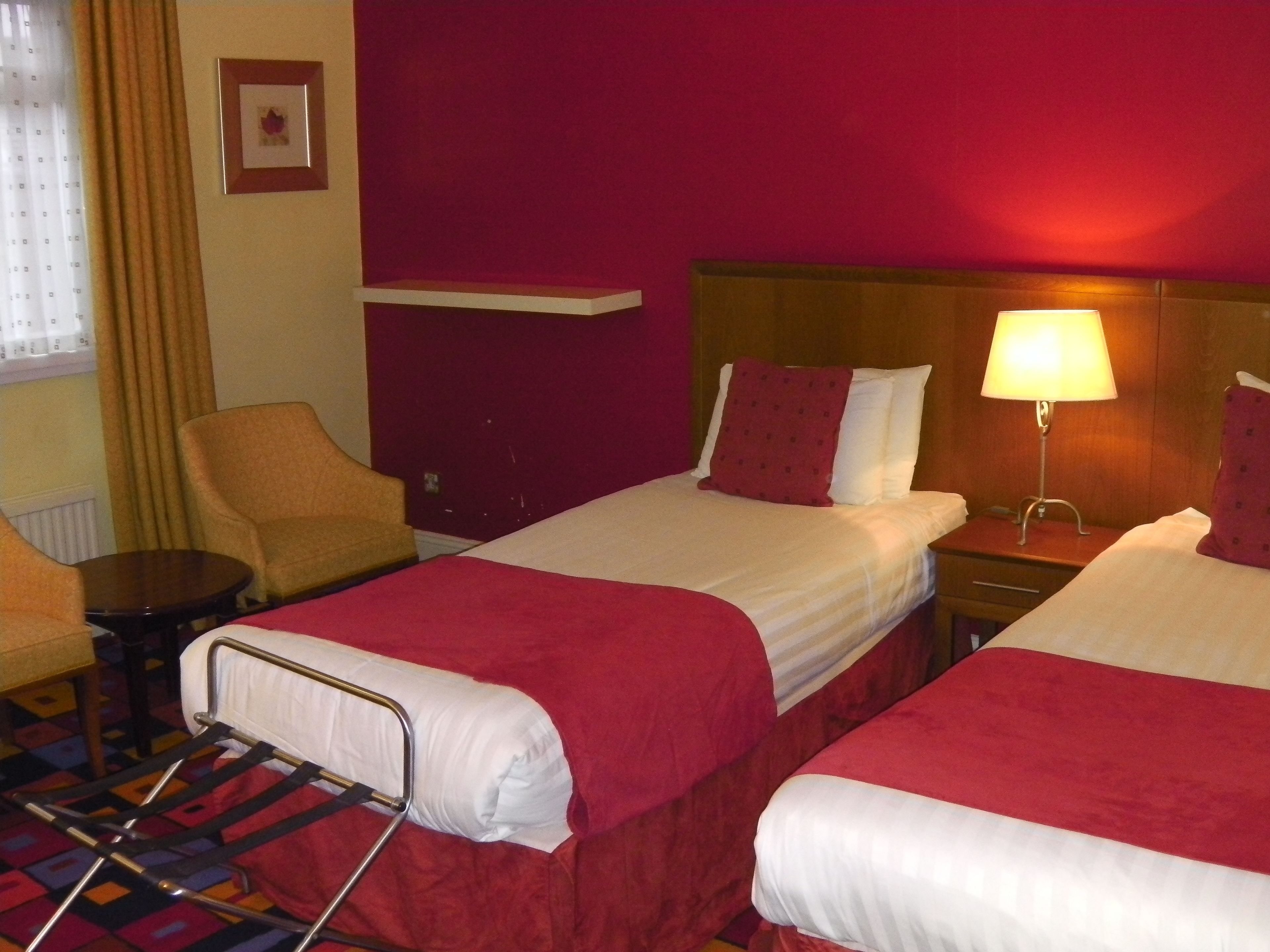 A hotel room with two beds, a chair, a table, and a lamp.