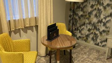 A hotel room with a round table, two yellow armchairs, a lamp, and a patterned wall.