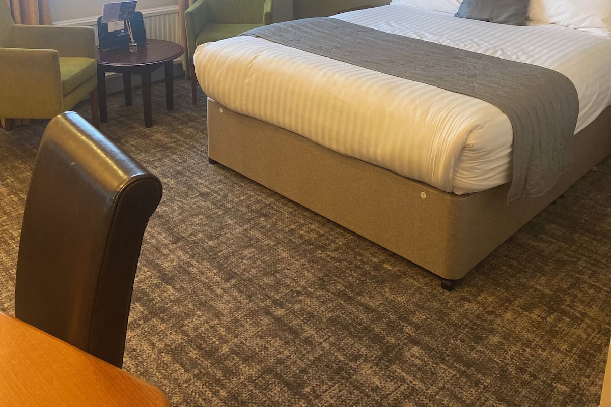 A hotel room with a large bed, a desk, a chair, and a window with curtains.