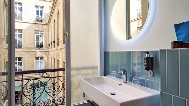 Un baño con un lavamanos blanco, un espejo redondo y azulejos azules.