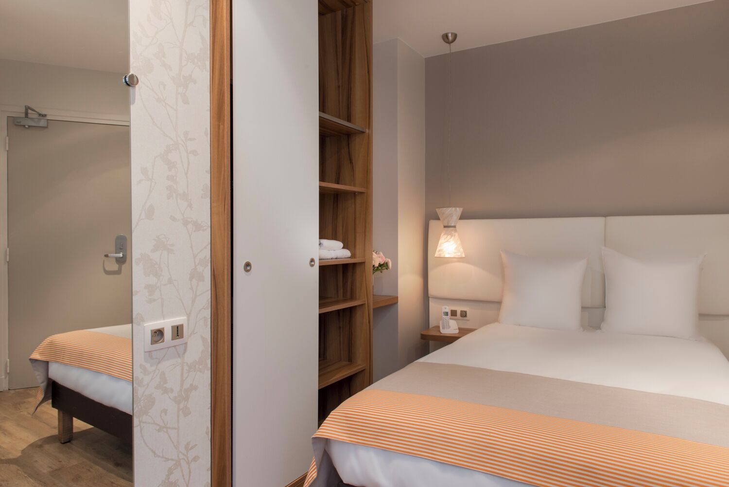 A hotel room with a bed, a bedside table with a lamp, a wardrobe, and a shower area.