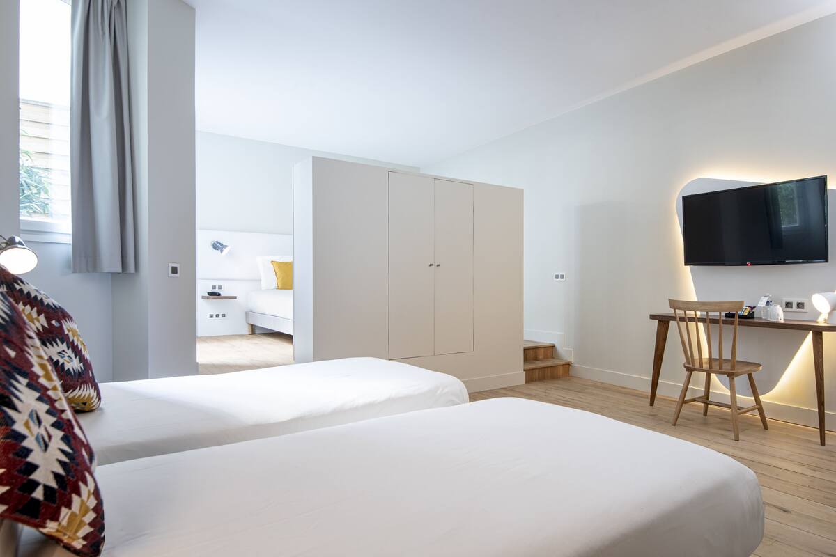 Una habitación de hotel moderna con dos camas, un escritorio con silla, un televisor montado en la pared y un armario.