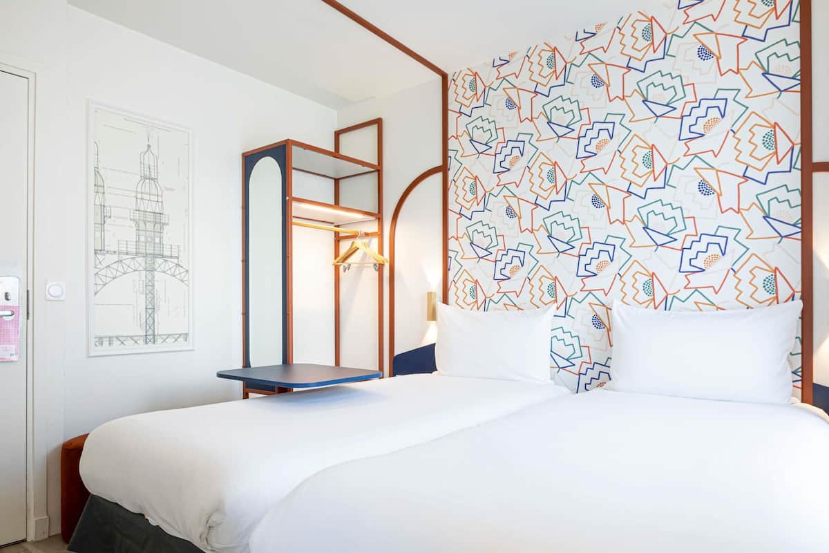 Une chambre d’hôtel avec un lit, une table de chevet en bois, un luminaire suspendu et un mur à motifs.