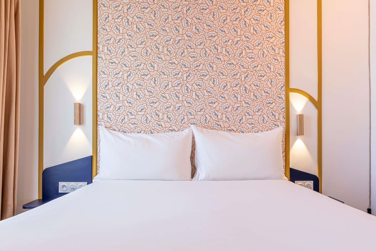 Un lit bien fait, avec une tête de lit à motifs, des lampes de chevet et une prise électrique sur la table de chevet.