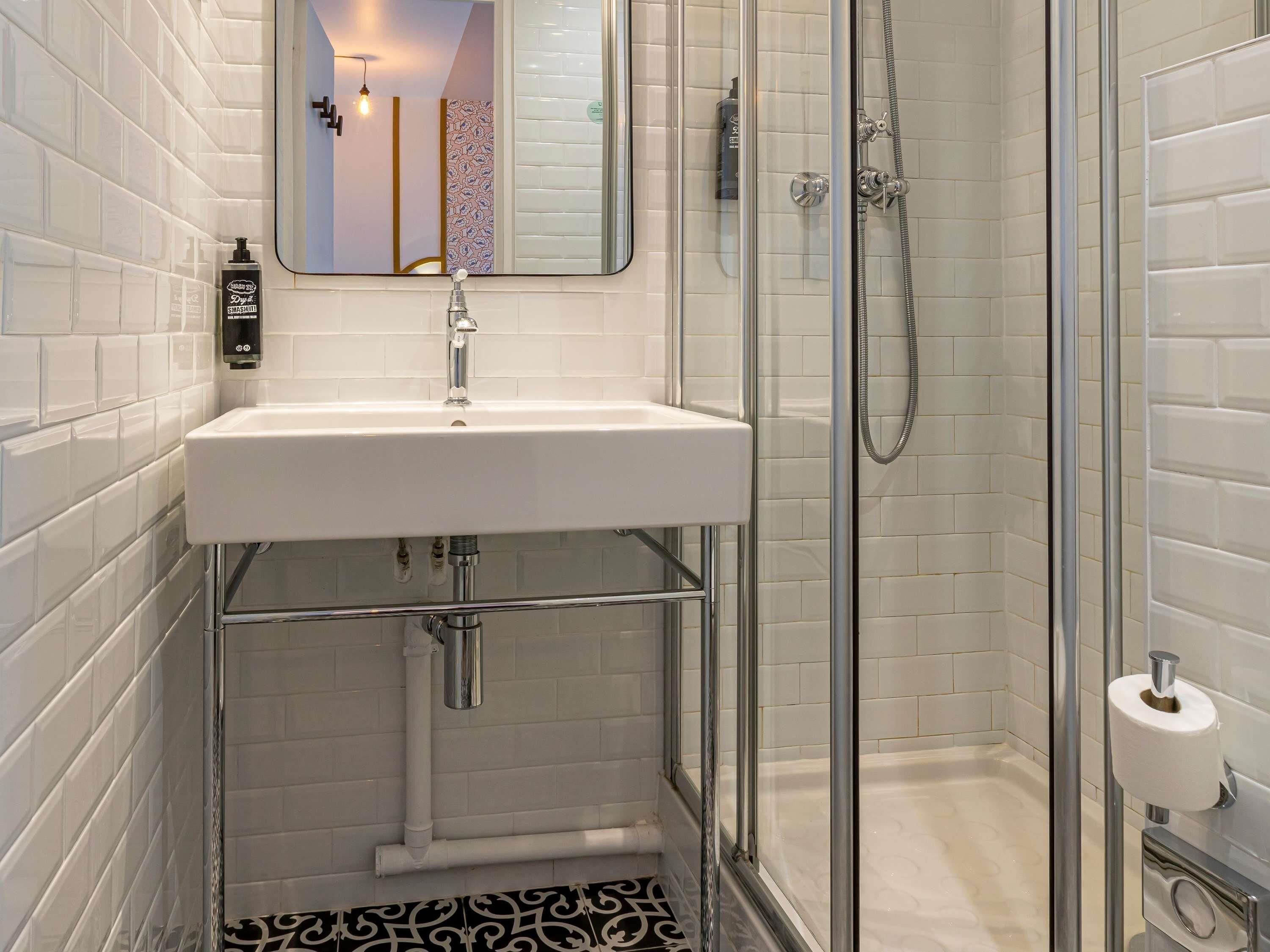 A modern bathroom with a white sink, glass shower enclosure, and a toilet paper holder.