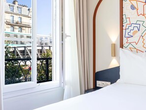 A hotel room with a large window, a bed, a nightstand, and a wall-mounted light fixture. - ibis Styles Paris Eiffel Cambronne (Paris)