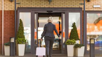 A person in business attire walking towards a building entrance with a suitcase.